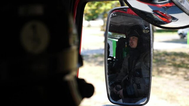 Young fireman reflecting in side mirror of moving big truck. Professional firefighter in full equipment riding on fire engine to an emergency. Concept of saving lives and heroic profession. Close up