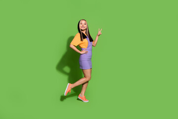 Full length photo of lovely young lady v-sign show dressed stylish violet yellow garment isolated on green color background