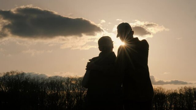 Two farmers in a field look forward at the setting sun, a man hugs a woman