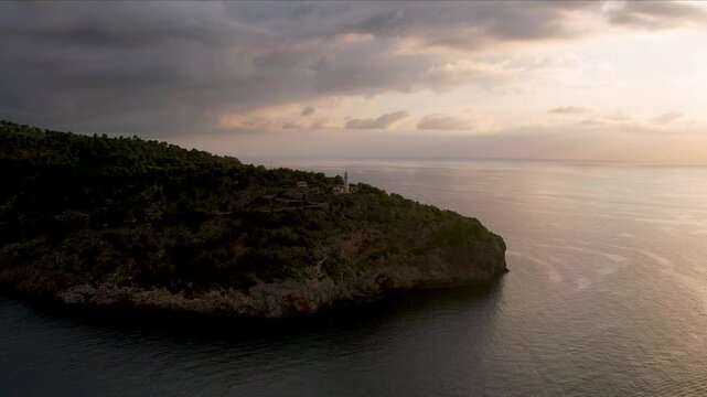 4K Aerial Drone video of popular summer destination, sunset over the cliffs with a lighthouse and a huge port of boats anchored at golden hour with seagulls flying. Port de Soller, Mallorca