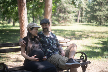 Young couple in the park. Pregnant wife and husband sitting on a bench in the park.