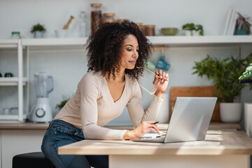Cheerful attractive woman working with laptop in the kitchen at home.