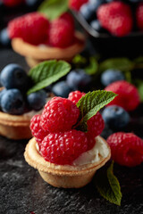 Small tartlets with fresh raspberries and blueberries on a black background.