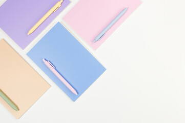 Top view of pink, purple, blue and beige notebooks on white background. Colorful pens, school, office wallpaper. Flat lay, copy space.