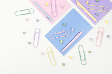 Top view of pink, purple and blue notebooks on white background. Colorful pens, paperclips, pins, school, office wallpaper. Flat lay, copy space.