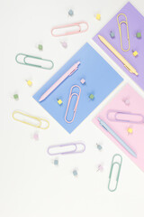 Top view of pink, purple and blue notebooks on white background. Colorful pens, paperclips, pins, school, office wallpaper. Flat lay, copy space.