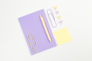 Top view of purple notebook on white background. Sticky note, paperclips, pen and pins. School, office wallpaper. Flat lay, copy space.