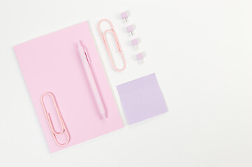 Top view of pink notebook on white background. Sticky note, paperclips, pen and pins. School, office wallpaper. Flat lay, copy space.