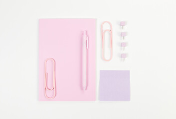Top view of pink notebook on white background. Sticky note, paperclips, pen and pins. School, office wallpaper. Flat lay, copy space.