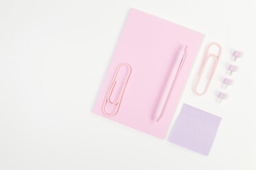 Top view of pink notebook on white background. Sticky note, paperclips, pen and pins. School, office wallpaper. Flat lay, copy space.