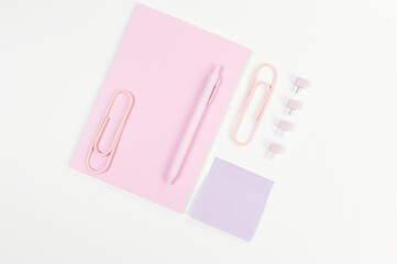 Top view of pink notebook on white background. Sticky note, paperclips, pen and pins. School, office wallpaper. Flat lay, copy space.