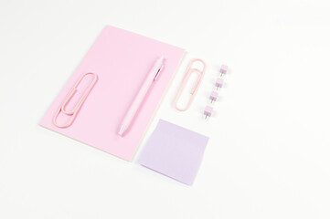 Top view of pink notebook on white background. Sticky note, paperclips, pen and pins. School, office wallpaper. Flat lay, copy space.