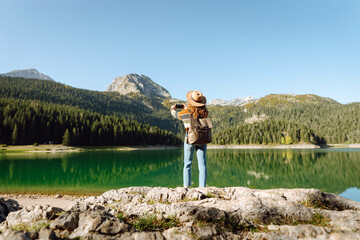 Obraz premium Young traveler is resting and taking pictures of amazing landscape with mountains and lake on smartphone during vacation. Tourism, nature, blogging concept.