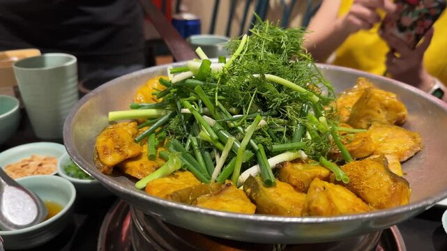A professional chef using chopsticks to adds cilantro and spring onion to the traditional and popular dish of boneless grilled hemibagrus fish, known as Cha Ca Hanoi, a fried river catfish.