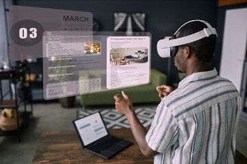 Modern young Black man wearing VR headset standing in living room using time management apps to plan his daily life