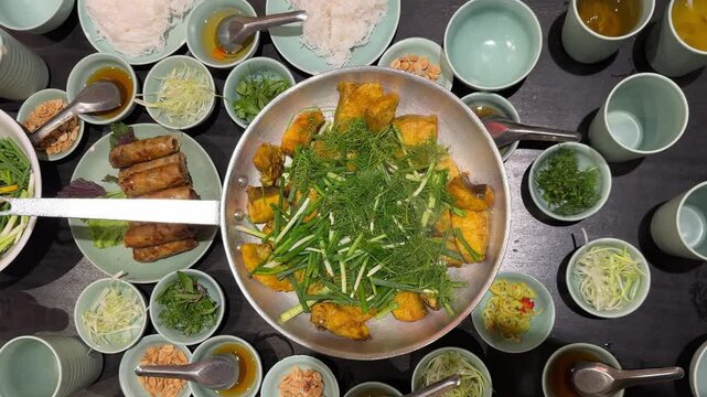Vietnamese fried spring rolls Cha Gio, with a dish of boneless grilled hemibagrus fish, river catfish fried called Cha Ca La Vong Hanoi, table of diners with fresh dill and spring onion, cilantro
