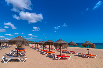 Beach umbrellas and sun loungers on sandy beach by blue sea and sky