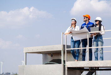 Group of engineers and architects working on the basis of a wind turbine Inspect the structure with the wind turbine in the background.