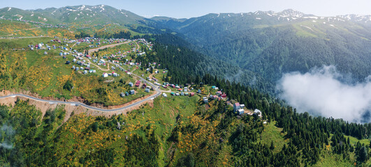 Aerial view of winding mountain road leading to scenic village of Gomismta, Georgia, nestled in lush forests and surrounded by dense fog layer or clouds, emphasizing the serene and secluded alpine