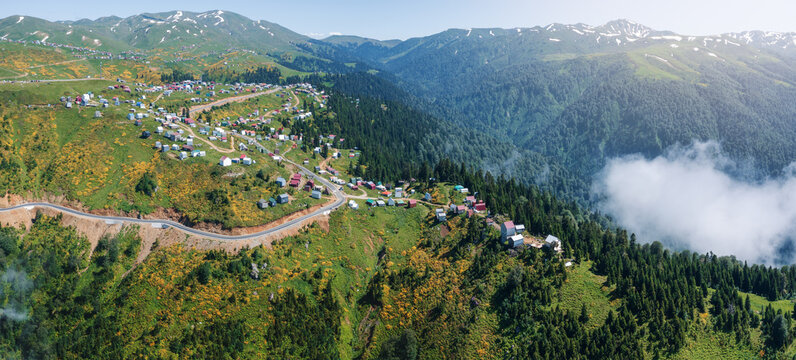Aerial view of winding mountain road leading to scenic village of Gomismta, Georgia, nestled in lush forests and surrounded by dense fog layer or clouds, emphasizing the serene and secluded alpine