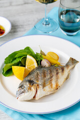 Grilled sea bream with vegetables and greens on wooden table
