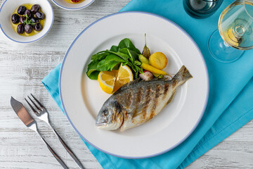 Grilled sea bream with vegetables and greens on wooden table