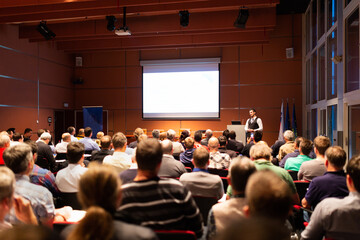 Speaker giving a talk in conference hall at business meeting event. Rear view of unrecognizable people in audience at the conference hall. Business and entrepreneurship concept.