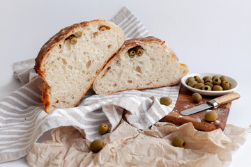 Freshly baked rustic artisan bread with green olives, presented on a striped cloth and wooden board