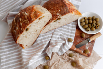Freshly baked rustic artisan bread with green olives, presented on a striped cloth and wooden board