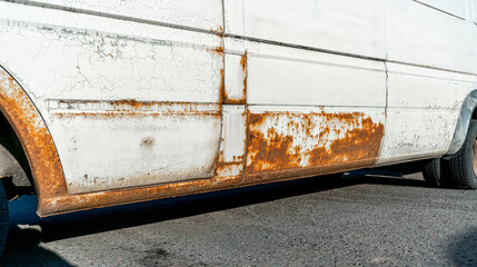 Rusty and damaged side of white van. Vehicle with visible rust and peeling paint on metal surface