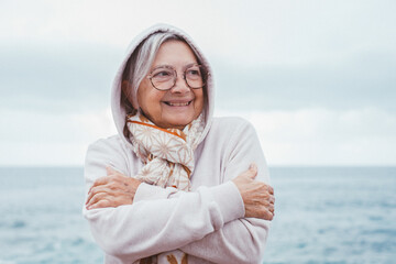 Portrait of attractive elderly woman smiling outdoors on a bad weather day at the seaside with sweater hood over her head to protect herself from the rain