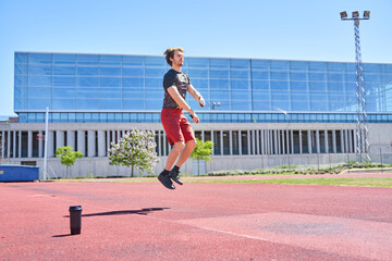 handsome sportsman training with jumping rope on the athletics track