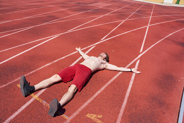 Tired young athletic lying on a running track after training