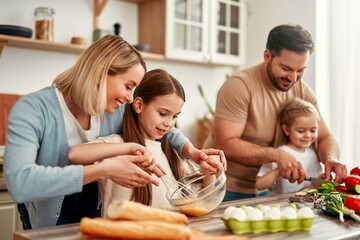 The family is joyfully cooking together in a welllit kitchen using fresh ingredients