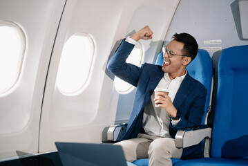 Young Asian executive excels in first class, multitasking with digital tablet, laptop and...