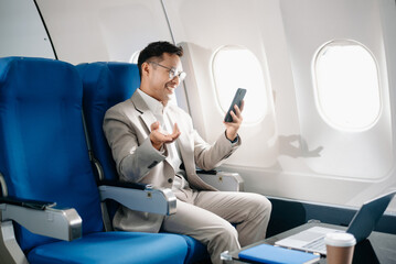 Young Asian executive excels in first class, multitasking with digital tablet, laptop and...