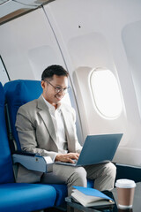 Young Asian executive excels in first class, multitasking with digital tablet, laptop and smartphone. Travel in style,