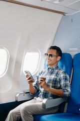 Asian male passenger of airplane sitting in comfortable seat while working laptop and tablet with mock up area using wireless connection. Travel in style,