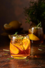 Iced tea or cocktail with ice, rosemary and lemon slices on the old brown table.