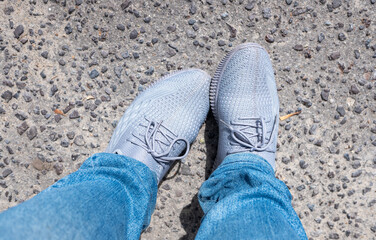 Feet in sneakers and jeans, top view of the ground.