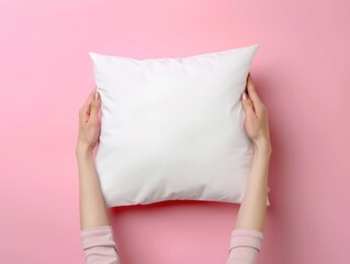 A person holding a white pillow on a pink surface
