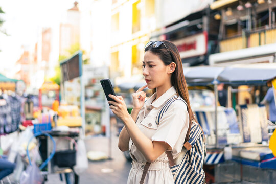 Young Asian woman getting lost and using map on a mobile phone while traveling and backpacker in Khaosan Road outdoor market in Bangkok, Thailand