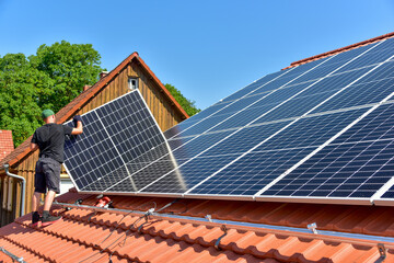 Dachdecker beim Aufbau einer Photovoltaikanlage auf einem neu gedeckten Ziegeldach: Das Schienensystem ist montiert und die Paneele werden auf das Schienensystem aufgesetzt