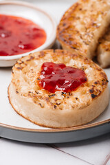 Hot Toasted Crumpets with piece of butter on a plate with strawberry jam. Perfect tasty breakfast popular in England, UK