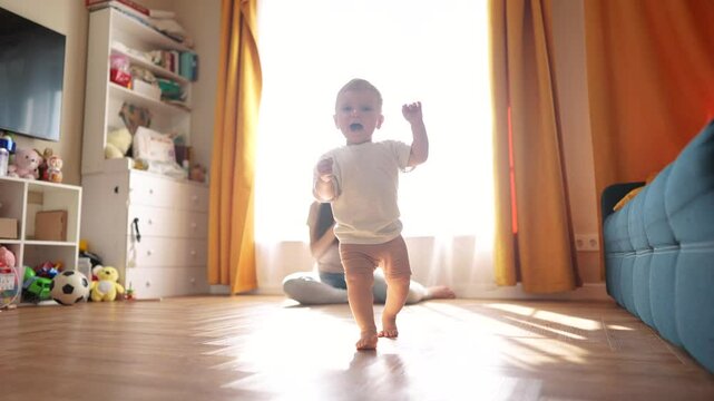 Family. The first steps to bringing your baby home. Child mother toddler family concept. Baby learns to walk indoors. A baby running on a wooden lifestyle floor with a woman.