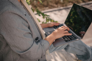 A person is sitting on a bench with a laptop open in front of them. They are typing on the keyboard, possibly working or browsing the internet. Concept of productivity and focus.