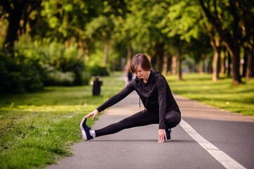 A young woman in black athletic wear stretching her legs on a park path before jogging. Emphasizing warm-up exercises and a healthy outdoor lifestyle.