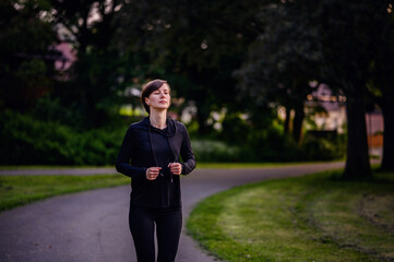 A young woman in black sportswear jogging in a park at dusk, showcasing determination and a healthy lifestyle.
