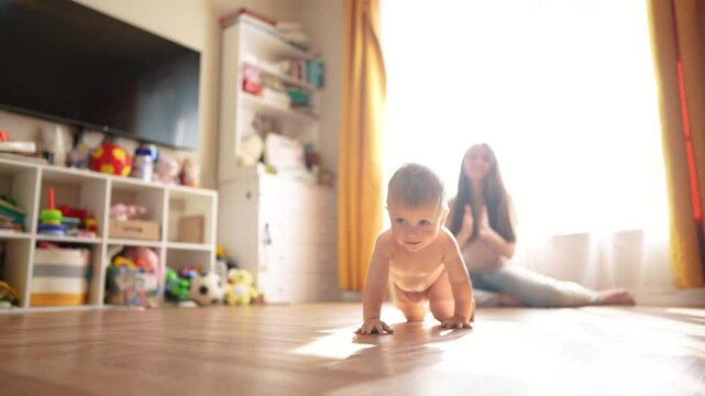 A mom teaches her baby to crawl. Child toddler walk concept. A baby crawls on the floor and takes the first steps. A mom teaches her baby how to crawl and how to do it in first few lifestyle steps.