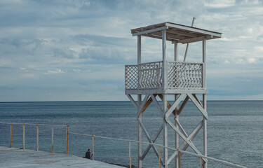 A lone lifeguard tower stands on a beach overlooking the calm, endless ocean under an overcast sky....